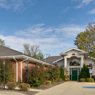 A healthcare clinic building with a brick exterior and green entrance, surrounded by trees under a clear blue sky.