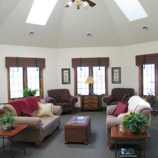 A cozy living room with multiple sofas, natural light from skylights and windows, and decorative plants.