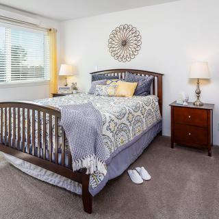 A cozy bedroom with a wooden bed frame, patterned bedding, and matching nightstands with lamps.