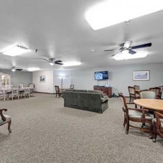 A spacious community room with seating areas, tables, a television, and ceiling fans.