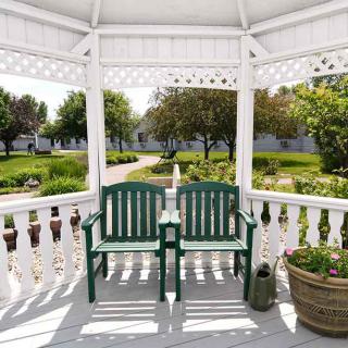 A peaceful view from inside a white gazebo with green benches overlooking a garden path.