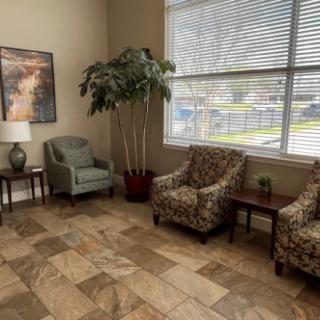 A cozy waiting room with chairs, a lamp, and a potted plant near a large window.