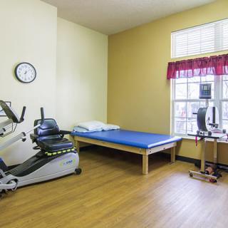 A rehabilitation room featuring a recumbent bike and an exercise mat, designed for physical therapy and fitness exercises.