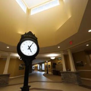A large clock stands in the center of a spacious lobby with high ceilings and warm lighting.