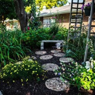 A tranquil garden with a stone pathway leading to a bench, surrounded by lush greenery and colorful flowers.