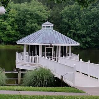 A serene gazebo situated by a tranquil pond, surrounded by lush greenery.