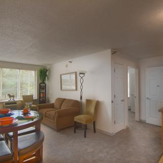 A cozy living room with a dining area, featuring a sofa, chairs, and a table near a large window.
