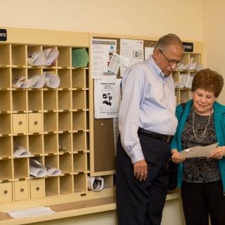 Two individuals review a document in an office mailroom.