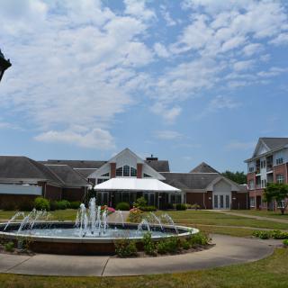 A scenic view of a building complex with a central fountain under a partly cloudy sky.