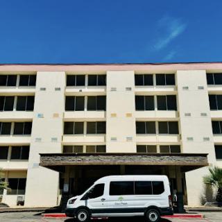 A hotel building with a white van parked in front under a clear blue sky.