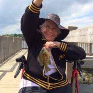 Person smiling while holding a fish on a dock.