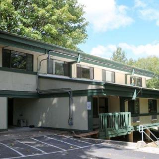 A two-story building surrounded by trees and a parking area.