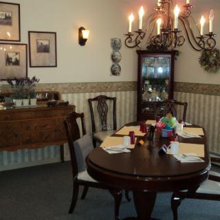 A cozy dining room with a set table, chandelier lighting, and classic wooden furniture.