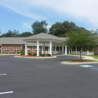 A single-story building with a large parking lot and surrounding greenery under a clear sky.
