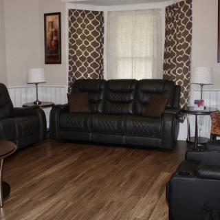 A cozy living room with black leather sofas, geometric patterned curtains, and a wooden floor.
