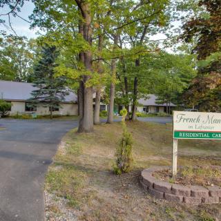 A residential property surrounded by trees with a driveway and a sign in the yard.