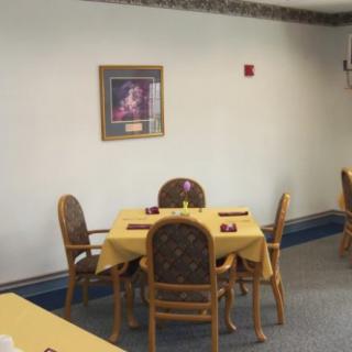 A small dining area with a table set for four, featuring yellow tablecloths and a framed painting on the wall.