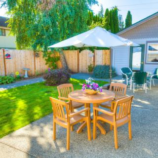 A cozy backyard patio with a wooden table and chairs under a large umbrella, surrounded by a well-maintained garden.