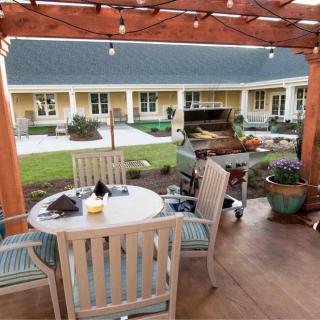 A cozy outdoor patio with a pergola and string lights, featuring a dining set overlooking a garden.