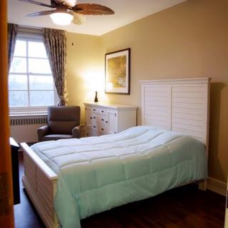 A cozy bedroom with a neatly made bed, armchair, dresser, and window with curtains.