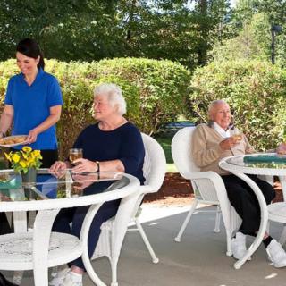 A group of seniors enjoying a relaxing day outdoors on a patio with a nurse assisting them.