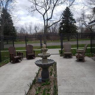 A quiet patio with a central fountain, surrounded by chairs and enclosed by a fence, set against a backdrop of trees.