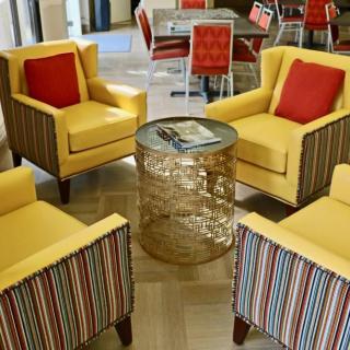 A vibrant seating area featuring yellow chairs with red pillows and a glass table.