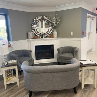 A cozy and modern seating area in a lobby, featuring stylish gray furniture around a decorative fireplace.