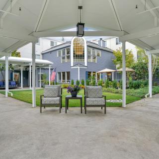 A view of a modern house with a spacious backyard patio, featuring lawn chairs and a well-maintained garden.
