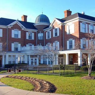 A symmetrical, historic brick building with a dome, surrounded by well-maintained landscaping.