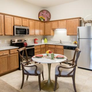 A cozy kitchen with wooden cabinets, modern appliances, and a small dining table set for two.