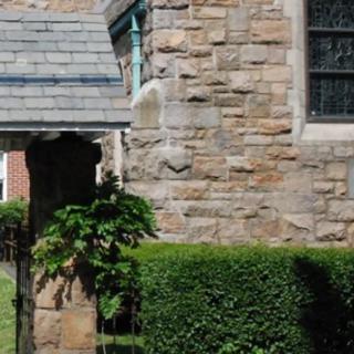 A stone church building with a hedge and a decorative window.