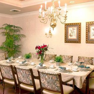 An elegantly decorated dining room with a long table set for guests, featuring a chandelier and floral centerpiece.