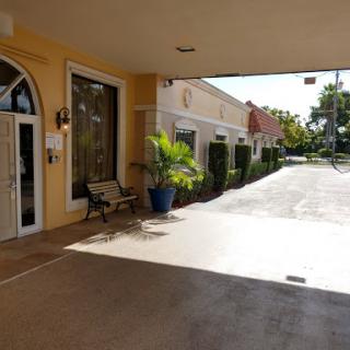 A sunny entrance to a commercial building featuring a walkway and greenery.