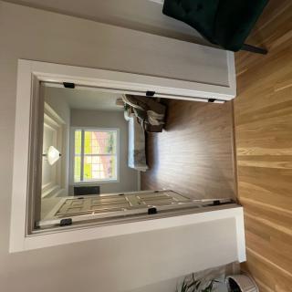 A view through a doorway into a bedroom with a bed, window, and wooden flooring.