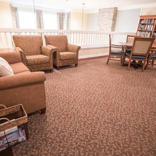 A cozy living room with armchairs, a carpeted floor, and a bookshelf.