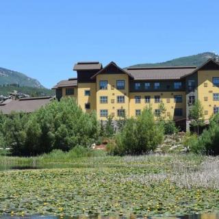 A scenic view of a large building surrounded by lily pads and trees, set against a backdrop of mountains.