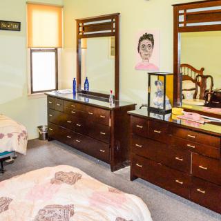A cozy bedroom featuring wooden dressers with mirrors and a neatly made bed.