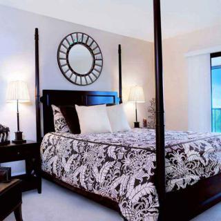 A stylish bedroom featuring a four-poster bed with patterned bedding, complemented by a decorative mirror and elegant nightstands.