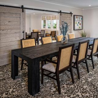 A stylish dining room featuring a long dark table, cushioned chairs, and decorative elements including a vase and patterned carpet.