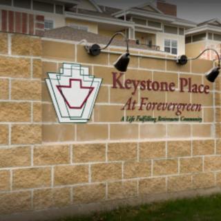 A sign for Keystone Place at Forevergreen, a senior living community, mounted on a stone wall outside a building.