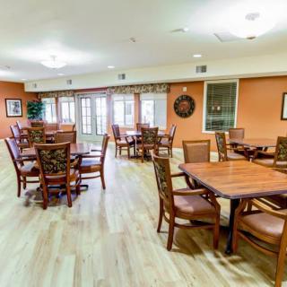 A spacious dining area with multiple tables and wooden chairs, featuring bright lighting and a warm atmosphere.
