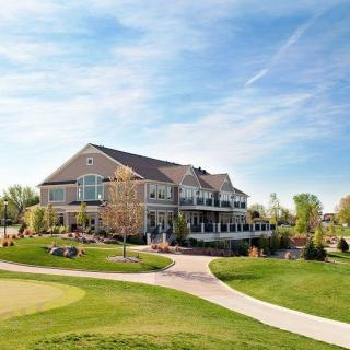 A scenic view of a clubhouse surrounded by a well-maintained golf course, with clear blue skies overhead.