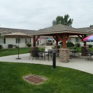 A well-maintained outdoor area featuring a gazebo with tables and chairs on a patio, surrounded by a lush lawn.