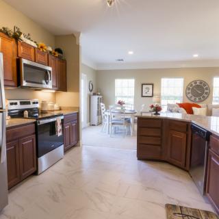 A modern kitchen with wood cabinets and stainless steel appliances, featuring an open layout leading to a dining area.
