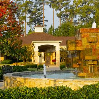 A scenic outdoor view featuring a fountain in front of a building surrounded by lush greenery and trees.