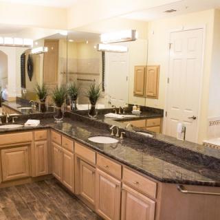 A spacious bathroom featuring a double vanity with granite countertops, large mirrors, and elegant lighting.