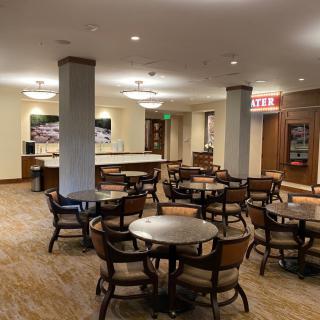 An indoor dining area with multiple tables and chairs, featuring a service counter in the background.