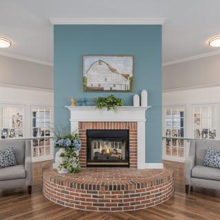 A cozy living room with a brick fireplace and blue accent wall, flanked by comfortable armchairs and elegant decor.