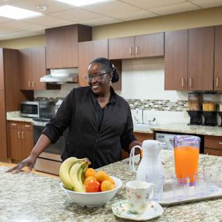 A cheerful woman enjoying her time in a well-equipped kitchen, surrounded by fresh fruits and beverages.